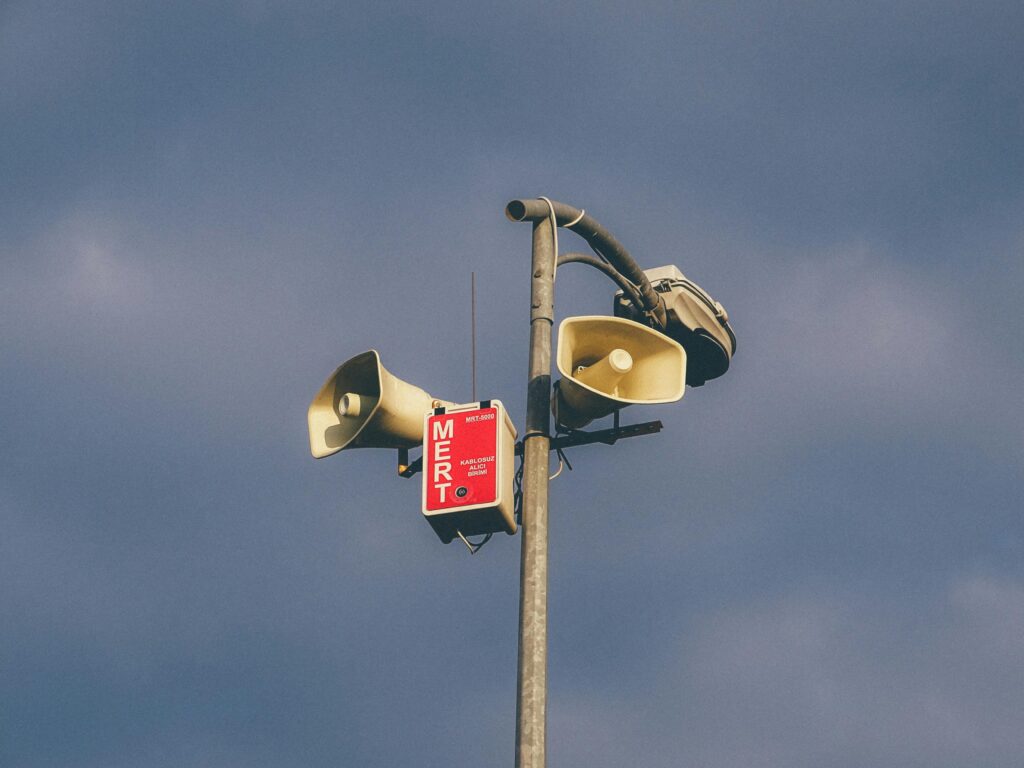 A warning system with loudspeakers on a pole against a cloudy sky, signaling emergency alerts.
